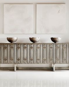 three silver bowls sitting on top of a metal cabinet in front of two white paintings