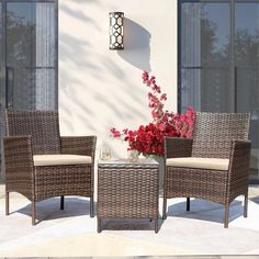 two wicker chairs and a table with flowers on it in front of a building