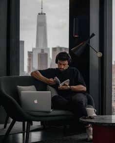 a man sitting on a couch in front of a laptop computer while reading a book