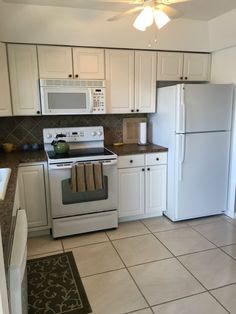 a kitchen with white cabinets and tile flooring, including a stove top oven next to a refrigerator