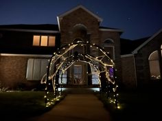 a lighted archway in front of a house at night with lights on the walkway and windows