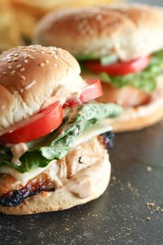 two grilled chicken sandwiches with tomatoes, lettuce and tomato on them sitting on a table