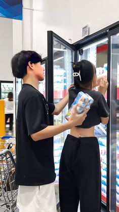 two people standing in front of a refrigeration unit with drinks and snacks