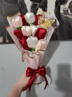 a hand holding a bouquet of flowers in front of a cow wall hanging on the wall