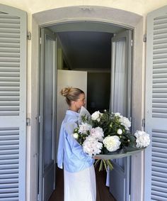 a woman holding a bouquet of flowers in front of an open door with shutters