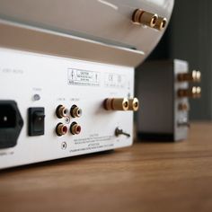 two audio devices sitting side by side on a wooden table with other electronic equipment in the background