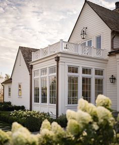 a white house with lots of windows and flowers in the foreground, on a sunny day