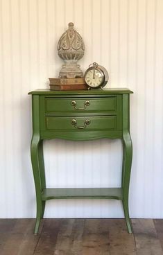 a green table with two drawers and a clock on top, against a white wall