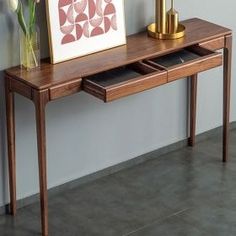 a wooden table with two drawers and a painting on it next to a vase filled with flowers