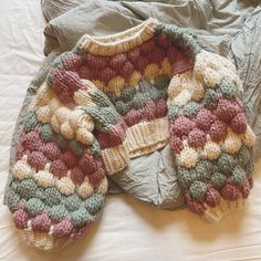 two knitted sweaters sitting on top of a bed