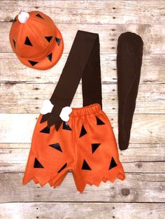 two pieces of clothing and a hat are laid out on a wooden surface, including a pumpkin costume