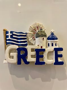 a sign that says greece with a windmill and flag in the background on a white wall