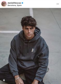 a young man sitting on the ground with his hands in his pockets and wearing a hoodie