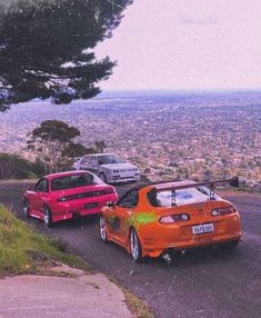 three cars parked on the side of a road next to a hill with trees and hills in the background