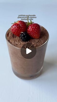 a cup filled with chocolate pudding and two strawberries on top of it, sitting on a white surface