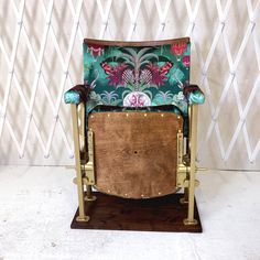 a wooden chair with green and pink fabric on it's back, sitting in front of a white wall