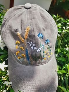 a gray hat with embroidered flowers on it sitting in the grass next to some bushes