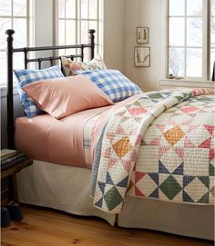 a bed with pink sheets and pillows in a bedroom next to two windows on either side of the bed