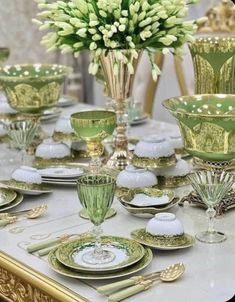 a table topped with lots of green and white dishes covered in gold trimmings