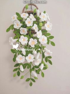 white crocheted flowers hanging from a wall with green leaves and branches in the center