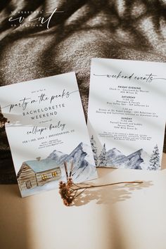 two wedding cards sitting on top of a bed next to a pine tree and mountain