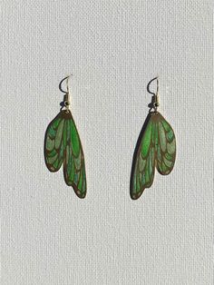 Shimmery shades of green resin in a brass wing shaped setting. Golden hypoallergenic earring hooks are made of 925 silver-plated copper. Each piece is handmade and is created by carefully pouring and mixing resin into each individual section. This tedious process leads to beautiful vibrant colors that imitate a stained glass look in a much more durable and lightweight way. Every piece is naturally unique as it is impossible to maintain the pigment to resin ratio, leading to large variations of c Nature-inspired Green Jewelry With Ear Wire, Unique Green Pierced Earrings, Green Hand Painted Drop Earrings, Unique Green Nickel-free Earrings, Unique Green Butterfly Earrings, Nickel-free Green Leaf-shaped Jewelry, Handmade Green Leaf-shaped Earrings, Nature-inspired Green Butterfly Jewelry, Green Butterfly Nature-inspired Jewelry