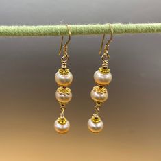 Unique presentation of peach freshwater pearls, antique gold spacers, and filigree bead caps in these elegant dangle earrings. The dangles are connected to each other and to the gold filled earwire through gold filled wrapped loops.  The earrings are about 1 1/4 inches long, measured from the earwire, and come nestled comfortably on a bed of cotton in a white cardboard box. Made in the USA by me. NA-821-0624-1111 Pearl Earrings With Gold Beads For Gift, Gold Beaded Pearl Earrings, Gold Pearl Earrings With Gold Beads, Gold Beaded Earrings With Pearl Drop For Gifts, Gold Pearl Drop Beaded Earrings For Gift, Gold Earrings With Pearl Drop And Round Beads, Gold Earrings With Pearl Drop, Elegant Gold Pearl Earrings With Gold Beads, Handmade Gold Pearl Beaded Earrings