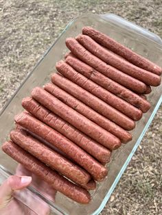 a person holding a glass dish full of hot dogs