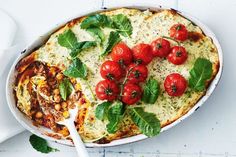 a casserole dish with tomatoes and spinach on top, next to a bowl of soup