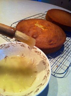 a bowl filled with liquid next to two muffins on a wire cooling rack