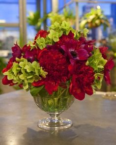 a vase filled with red and green flowers on top of a metal table next to plants