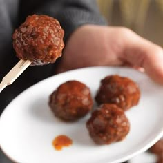 a person holding a plate with meatballs on skewers in their hand and dipping sauce on the other side