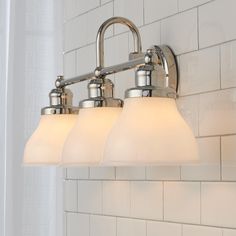 three light bathroom fixture with frosted glass shades on white tile wall behind shower curtain