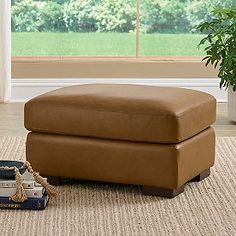 a brown ottoman sitting on top of a rug next to a window