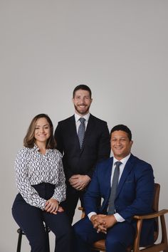 two men and a woman in business attire sitting on a chair smiling at the camera