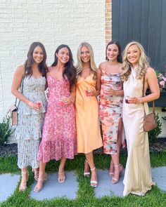 four women in dresses posing for a photo together on the front lawn of a house