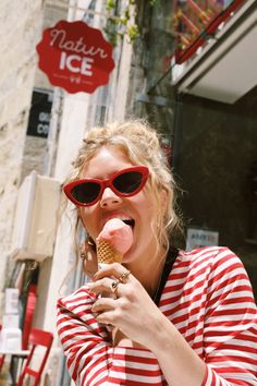 a woman eating an ice cream cone in front of a storefront with red and white striped shirts