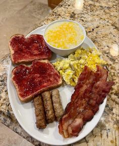 a plate with bacon, eggs, toast and cheese on it next to a bowl of mustard