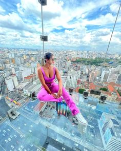 a woman sitting on top of a glass floor in the middle of a city with lots of tall buildings