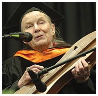 an older woman playing a musical instrument while wearing a graduation gown and holding a microphone