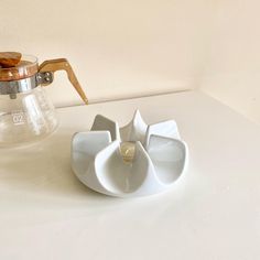 a coffee pot and saucer sitting on a white counter top next to a teapot