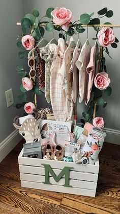 a wooden crate filled with baby items on top of a hard wood floor next to pink roses