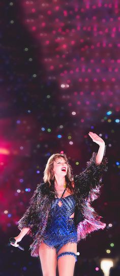 a woman in a blue and black outfit on stage with her arms out to the side