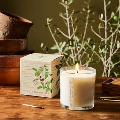 a candle sitting on top of a wooden table next to a box and some plants