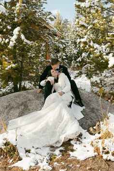 a bride and groom sitting on a rock in the snow