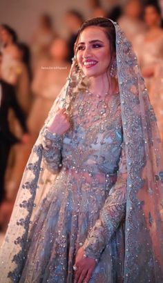 a woman in a wedding dress and veil smiles as she walks down the aisle with her hand on her hip