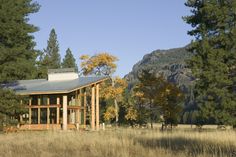 a log cabin sits in the middle of a field with tall grass and trees around it