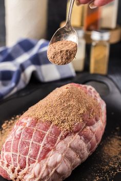 a person spoons seasoning from a piece of raw meat on a black plate