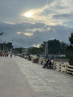 people are sitting on benches and walking down the sidewalk in front of some buildings with cloudy skies