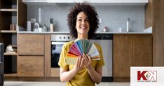 a woman holding a fan in her hands and looking at the camera while standing in a kitchen